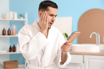 Shocked young man with hair loss problem and brush in bathroom