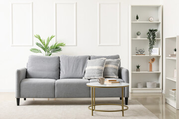 Naklejka premium Interior of light living room with grey sofa, table and shelf units