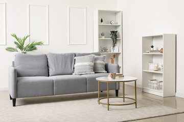 Interior of light living room with grey sofa, table and shelf units