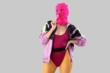 Beautiful young stylish woman in balaclava with lollipop on grey background