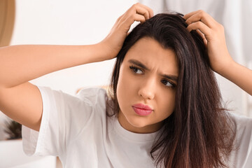 Fototapeta premium Stressed young woman examining her hair for dandruff in light bathroom