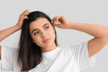 Fototapeta premium Young woman with dandruff problem examining her hair on white background