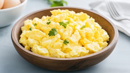 Scrambled eggs served in a wooden bowl garnished with fresh herbs on a light table surface.