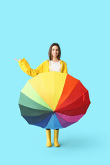 Young happy woman in raincoat with opened colorful umbrella on blue background