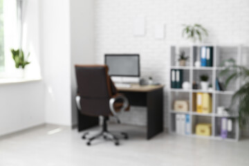 Interior of office with workplace, brown armchair, modern computer and shelving unit, blurred view