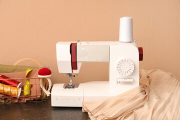 Modern sewing machine with tailor's supplies and fabric on beige background