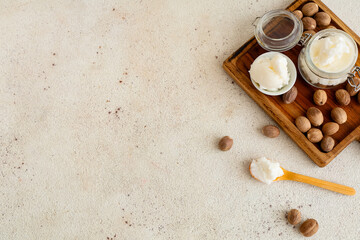 Wooden board with shea butter and nuts on light background