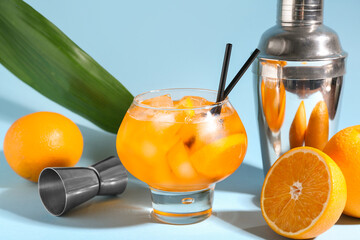 Glass of Aperol spritz cocktail with oranges and shaker on blue background
