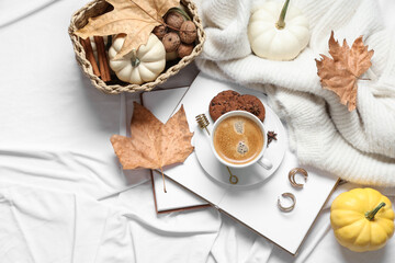 Cup of tasty pumpkin coffee with cookies, autumn decorations, books and warm sweater on bed at home