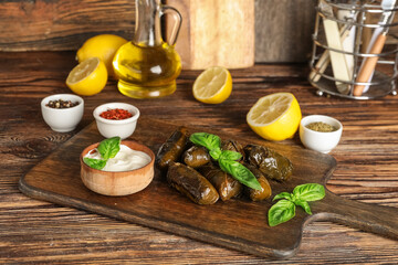 Cutting board with tasty Dolmas (stuffed grape leaves), sour cream, lemon and spices on wooden table
