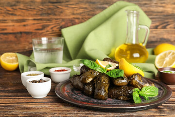 Plate with tasty Dolmas (stuffed grape leaves), lemon and spices on wooden table