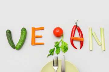 Word VEGAN made of fresh vegetables, plate and cutlery on grey background