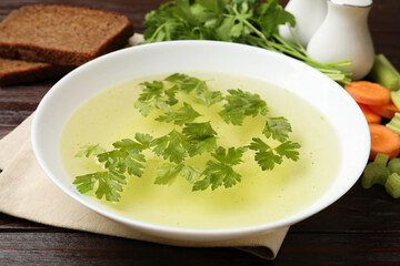 Tasty chicken bouillon with parsley in bowl on wooden table, closeup