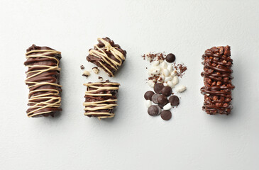 Delicious chocolate puffed rice bars and cacao chips on white table, flat lay