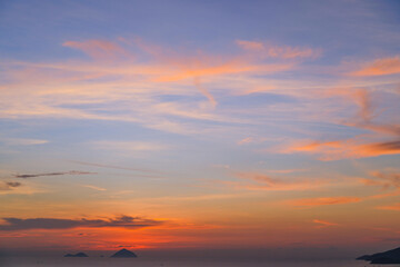 Cirrus evening clouds backlit by the sun, gradien orange blue sky view over the sea with islands horizon