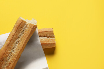 Paper bag with fresh baguette on yellow background, top view. Space for text