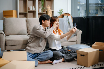 Young couple preparing for a move, packing boxes and a suitcase in a cozy living room. Perfect for...