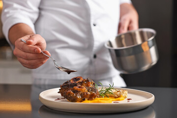 Professional chef adding sauce to delicious dish at table indoors, closeup