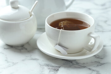 Tea bag in cup with hot drink on light marble table, closeup