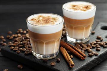Tasty latte macchiato in glasses, coffee beans and cinnamon on black wooden table, closeup