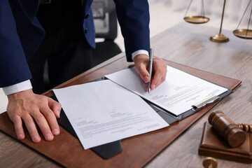 Notary signing document at wooden table in office, closeup