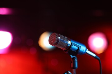 Obraz premium Microphone on stand against red background with blurred lights, space for text. Bokeh effect