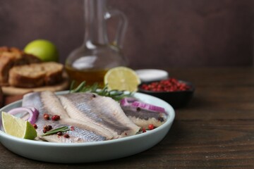 Marinated herring fillets with onion rings, rosemary, lime and peppercorns on wooden table,...