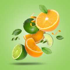 Lime, orange, zest and leaves in air on light green background