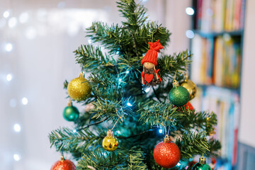 Figurine of a girl in a red hat hangs among the balls on a Christmas tree