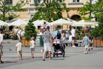 Joyful family outing in a bustling square during a sunny day, exploring together amidst cafe and lively atmosphere.