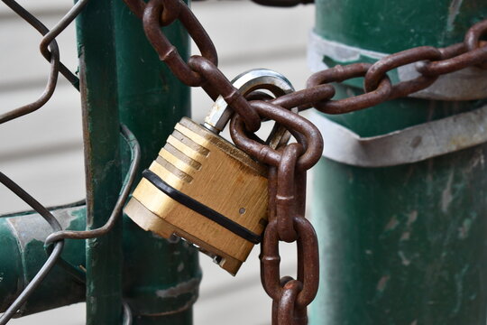 Gold colored lock on green gate. Locked chain prevents gate from opening.