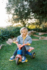 Little girl pedaling a tricycle on green grass in the park