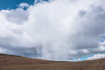 Alpine view to giant white cloud pours rain in large mountains. Awesome huge low cloud with rain poured down above high stone pass. Dramatic mountain landscape with big unusual rainy cloud in blue sky