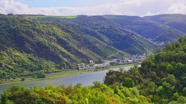 Aerial tracking view of beautiful rolling hills and small river side town during a sunny summer day in the Rhine River Valley, Germany