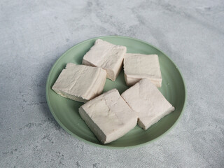 Tahu Putih or Tofu, one of raw ingredient food made from fermented soybean extract. Served in green plate with grey background. selective focus