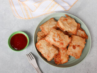 Tempe Kemul or Mendoan or fried tempeh with flour on a plate. Indonesian traditional snack, from fried tempeh with flour. Served with cayenne pepper. Street food snacks. gorengan