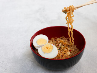 Instant fried noodle with boiled egg, chili and vegetable in red bowl on grey background. unhealthy food
