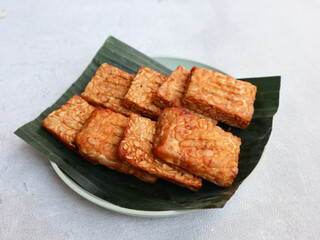 Tempe Goreng or Fried tempeh is a traditional food from Indonesia, made from fermented soybean seeds wrapped in banana leaves. served in a plate with banana leaves. Indonesian food