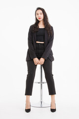 Fototapeta premium Portrait full body asian beautiful woman curly hair, wearing black suit, black long pants, model girl attractive confident, pose sitting on stool smiling look at camera on white background in studio.