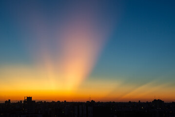 sunset with orange colored rays of sunlight against the blue sky, seen in Buenos Aires, Argentina