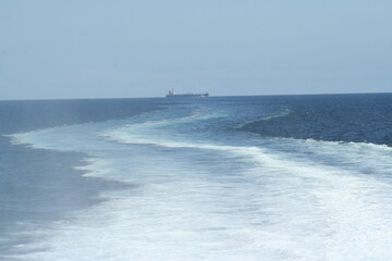 Wake of a ferry on the open sea, with a cargo ship in the background - Sillage d'un ferry en pleine...