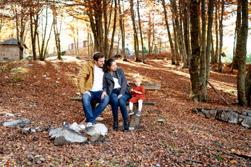 Fototapeta premium Hugging mom and dad look at a little girl sitting on a bench in the autumn forest