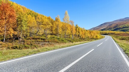Scenic Winding Road Through Vibrant Autumn Foliage Against Clear Blue Sky in Mountainous Landscape