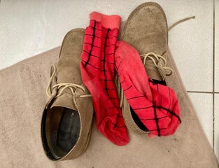 A pair of iconic South African veldskoen shoes and a pair of red socks discarded on a mat on the floor