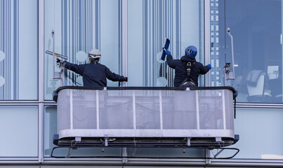 高層ビルのゴンドラに乗って窓拭きをする作業員 © captainT