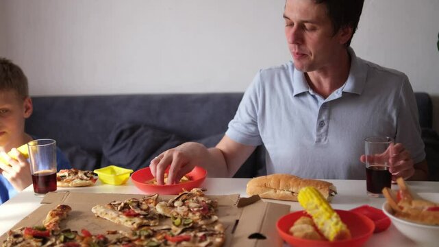 Caucasian kid boy and his father eating junk food at home. Single Father and son fast food, unhealthy food concept. Part of series