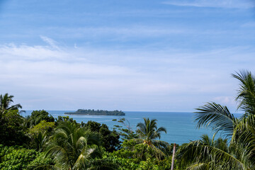 Lush tropical coastline of Gunuang Padang, Padang, West Sumatra, Indonesia, featuring a mix of vibrant green foliage and bare trees overlooking the calm blue ocean