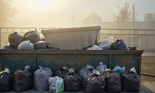 Overflowing dumpster filled with various trash bags, set in a smoggy, outdoor environment.