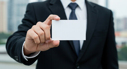 Close-up of a corporate man in a dark suit holding a blank white business card towards the camera, with a blurred cityscape in the background