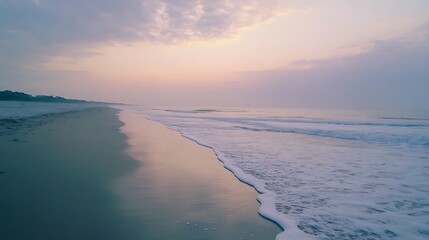 Serene sunrise over calm ocean waves gently lapping a tranquil sandy beach.